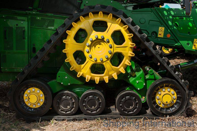 Close-up of a green and yellow agricultural machine's tread and wheels on a field.
