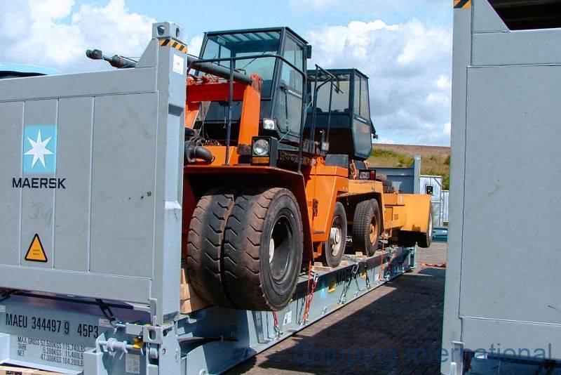 An orange vehicle is loaded on a shipping container, surrounded by other containers and a blue sky.