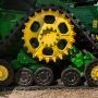 Close-up of a green and yellow agricultural machine's tread and wheels on a field.
