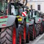 A row of tractors with large tires parked on a street, showcasing their distinctive green and gray designs.