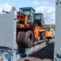 An orange vehicle is loaded on a shipping container, surrounded by other containers and a blue sky.