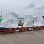 A container at a shipping yard with covered cargo and some workers, under a cloudy sky.